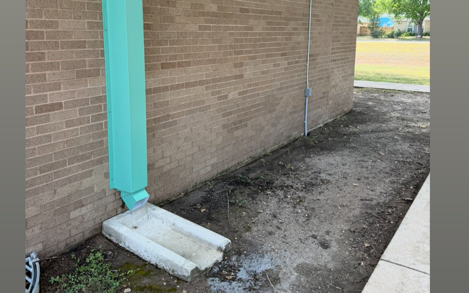 The same brick perimeter and downspout line near Austin TX after commercial exterior cleaning, with the masonry color restored