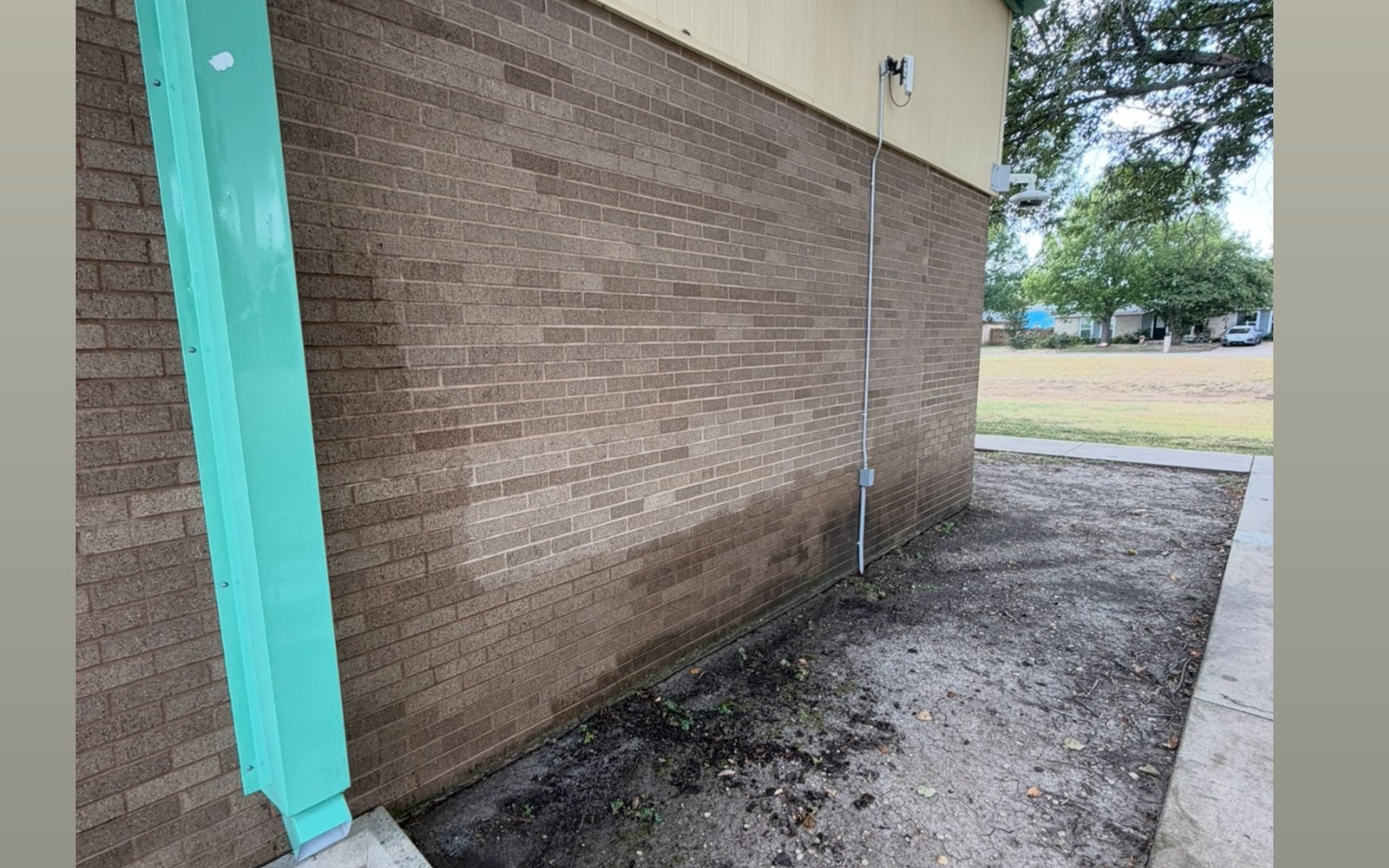 Brick building perimeter and downspout line in the Austin TX area with dirt and runoff staining before cleaning