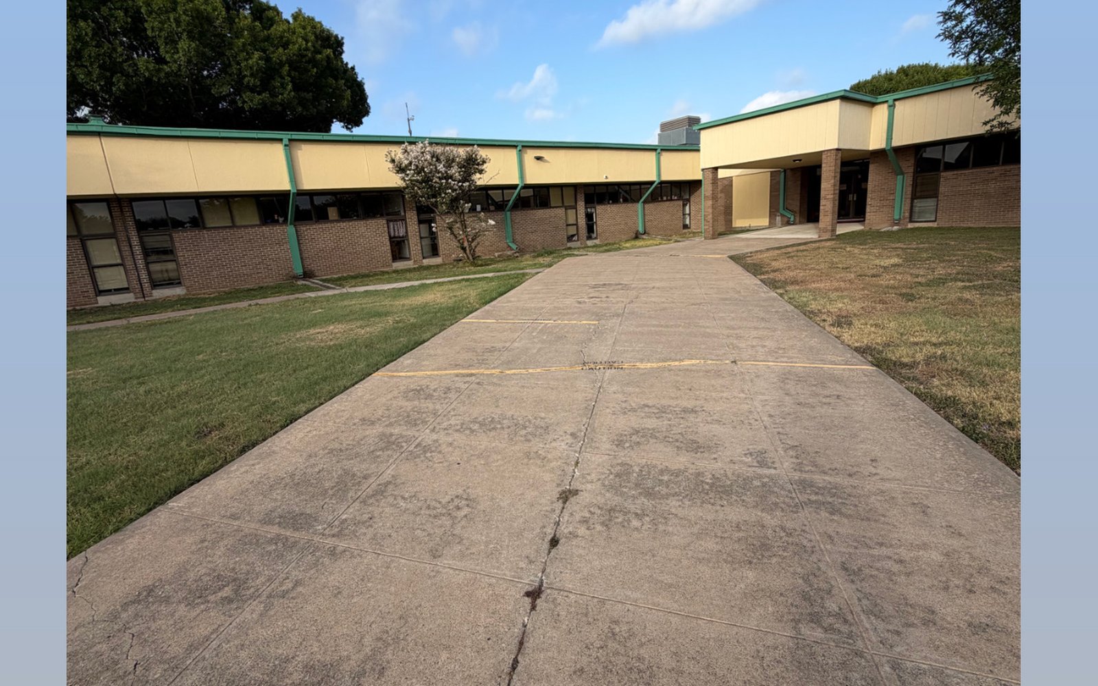 Wide commercial walkway at a Greater Austin TX building with grey traffic staining before pressure washing