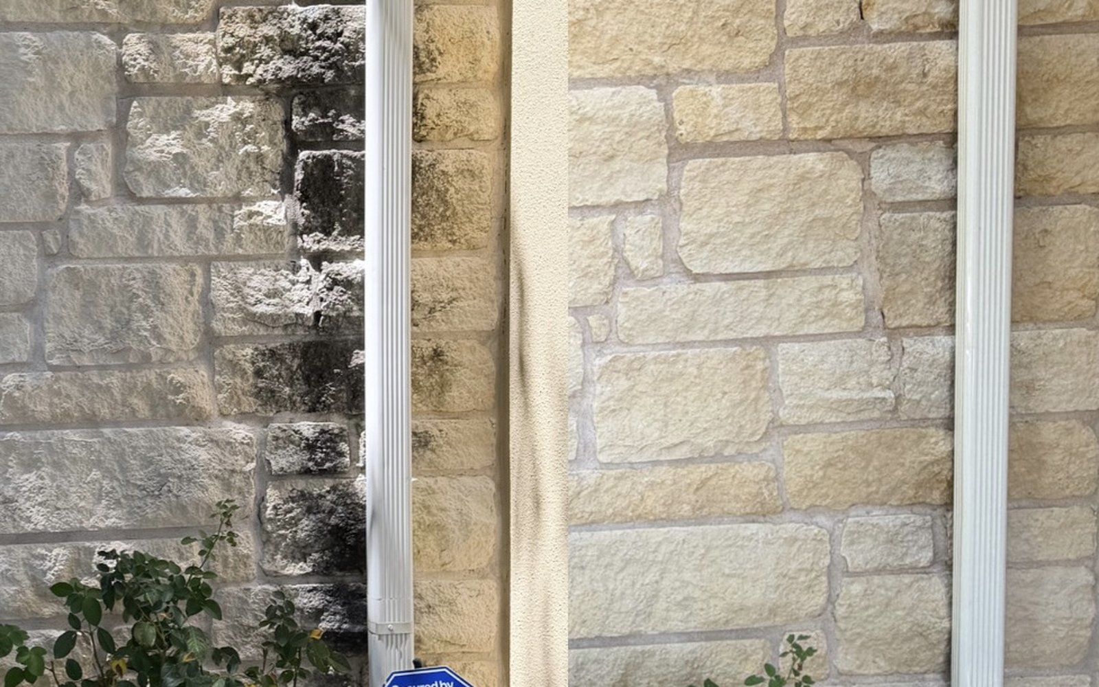 Limestone house wall in the Austin TX area with black algae staining on the left and the soft washed clean stone on the right